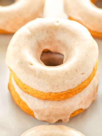 A stack of two pumpkin donuts. Additional donuts surround the stack.