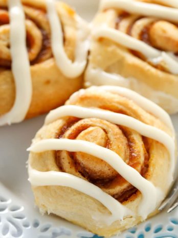 Three iced pumpkin cinnamon rolls on a white plate.