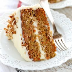 A slice of carrot cake on a decorative white plate. A fork rests on the side of the plate.