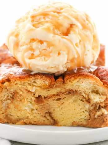 A slice of bread pudding topped with ice cream and caramel sauce on a white plate.