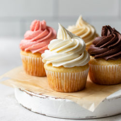 Four cupcakes topped with different flavors of buttercream frosting sitting on a rustic cake stand.