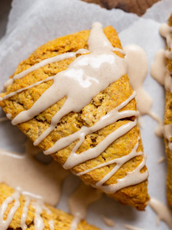 A pumpkin scone topped with maple cinnamon glaze on a piece of parchment paper.